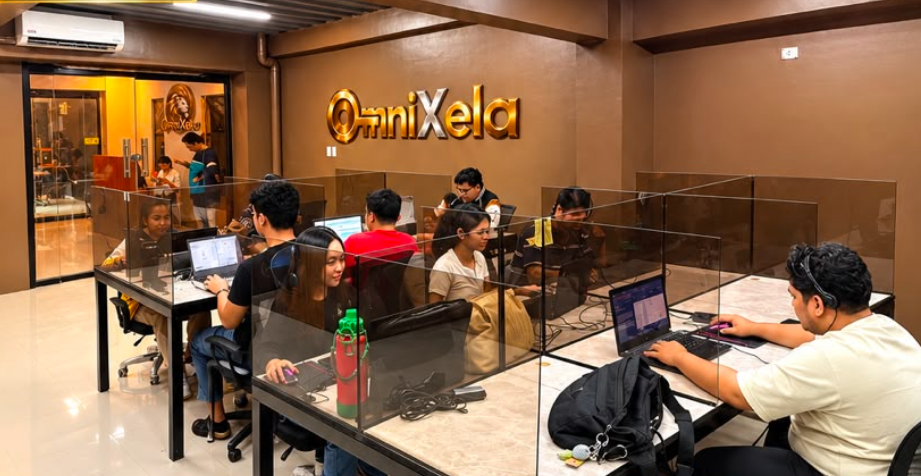 OmniXela production floor with agents working at partitioned desks under the gold OmniXela sign